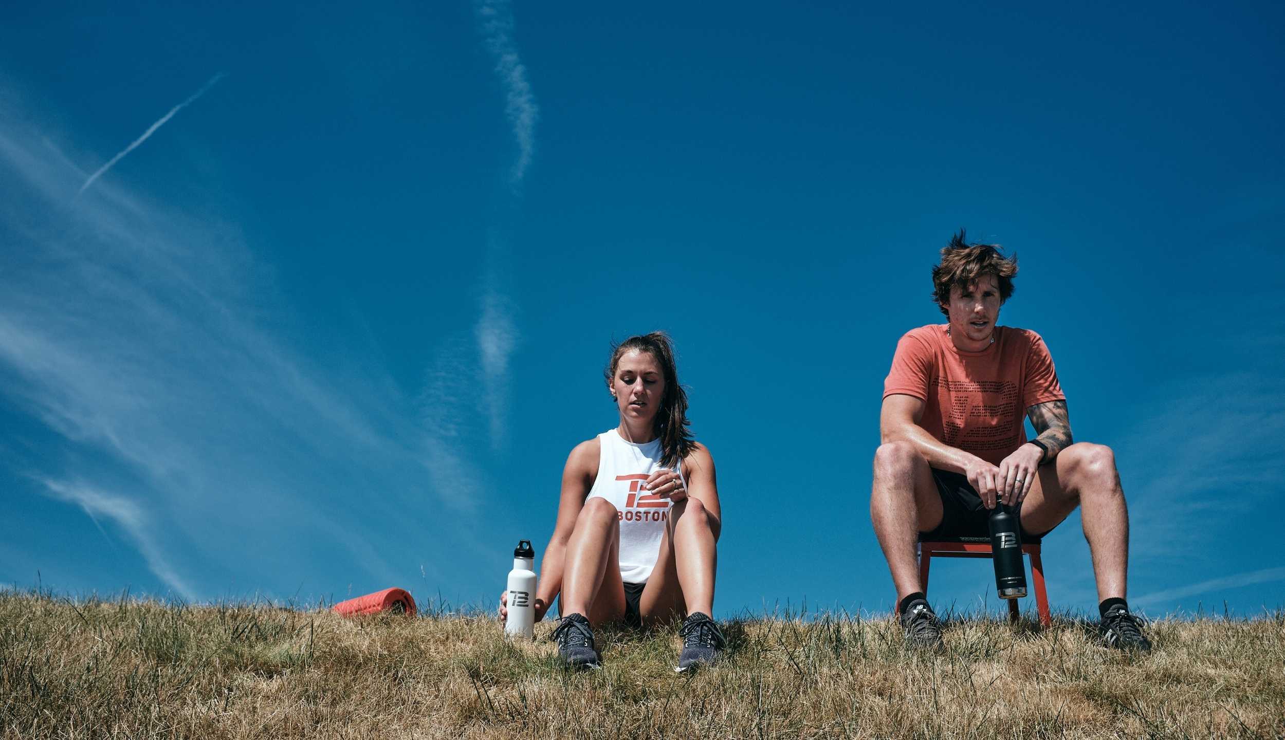 Two people sit on a hillside with water bottles.