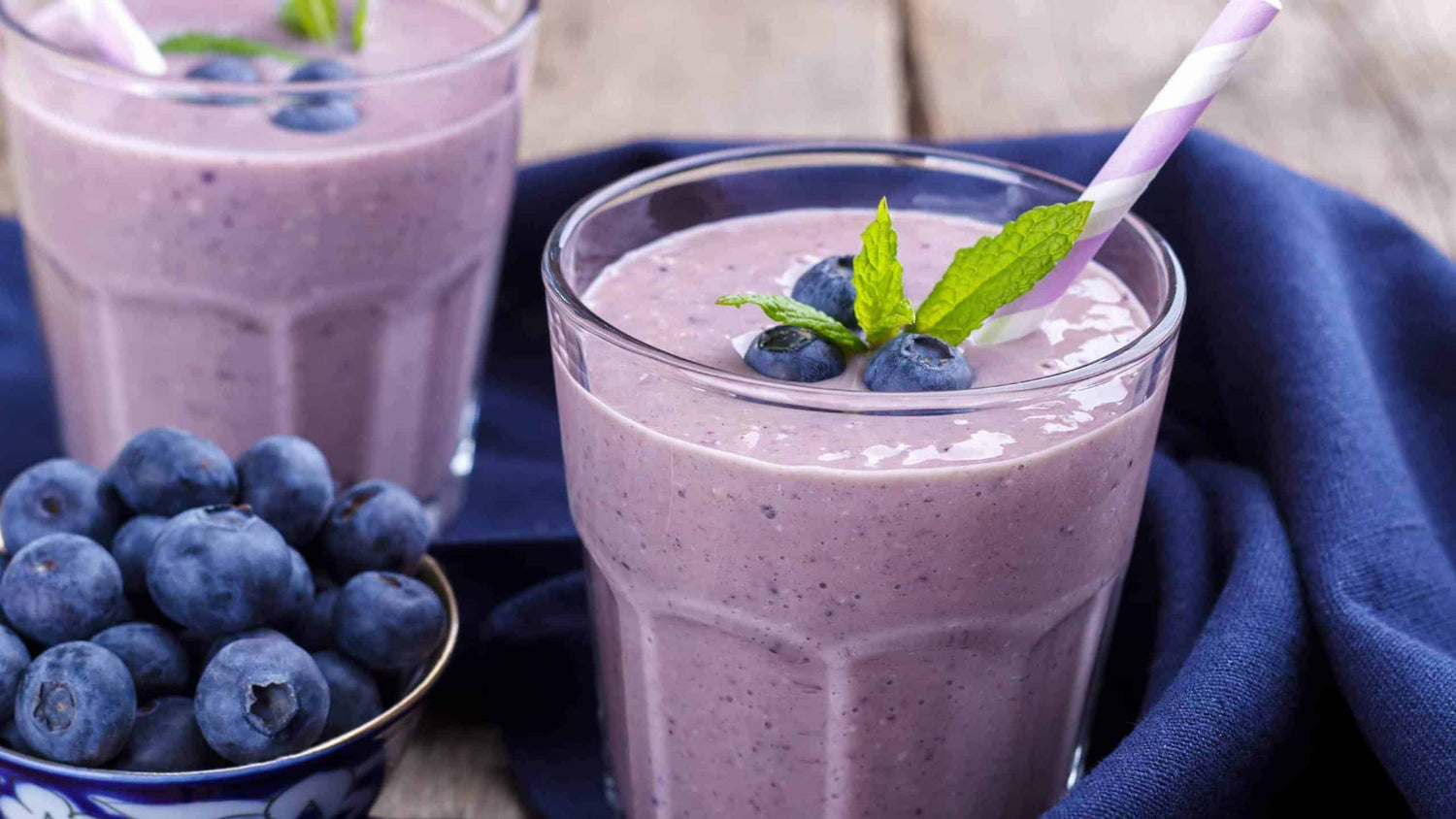 Photo of two glasses filled with purple smoothie and blueberries on the side