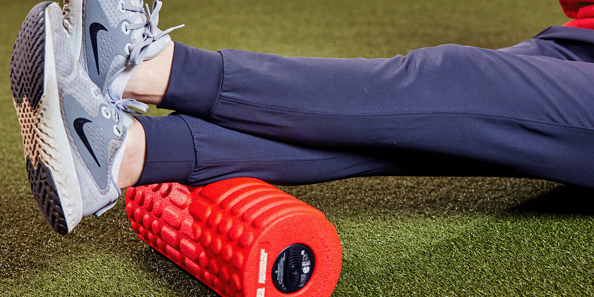 Person rolling out their calves with a foam roller on turf