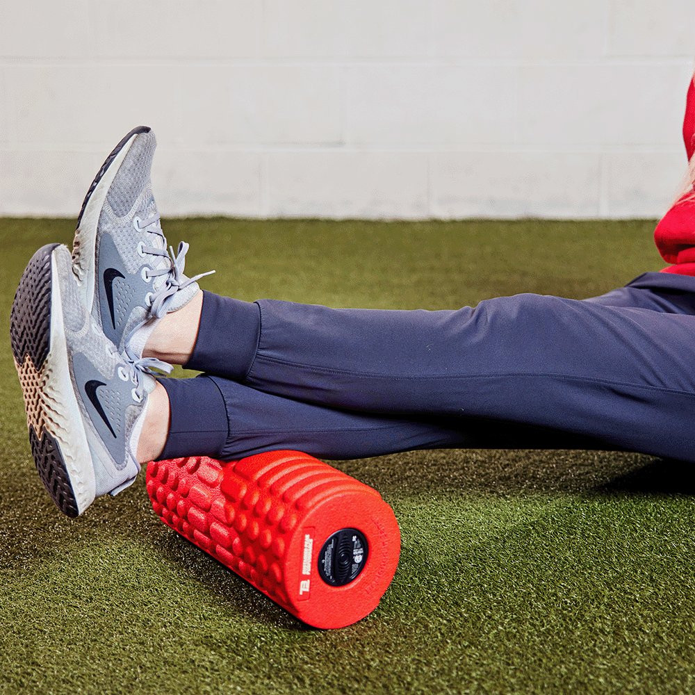 Man rolling his ankles on a foam roller on turf